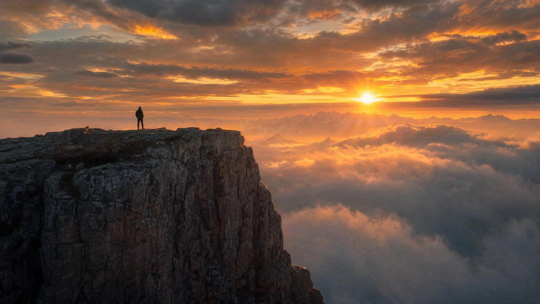 Epic cinematic landscape of a lone traveler standing on top of a massive mountain cliff during sunri